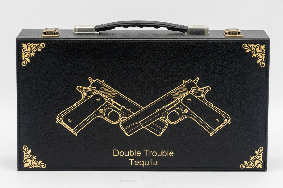 Black tequila box with gold embossed design of two crossed guns and 'Double Trouble Tequila' text on a white background.