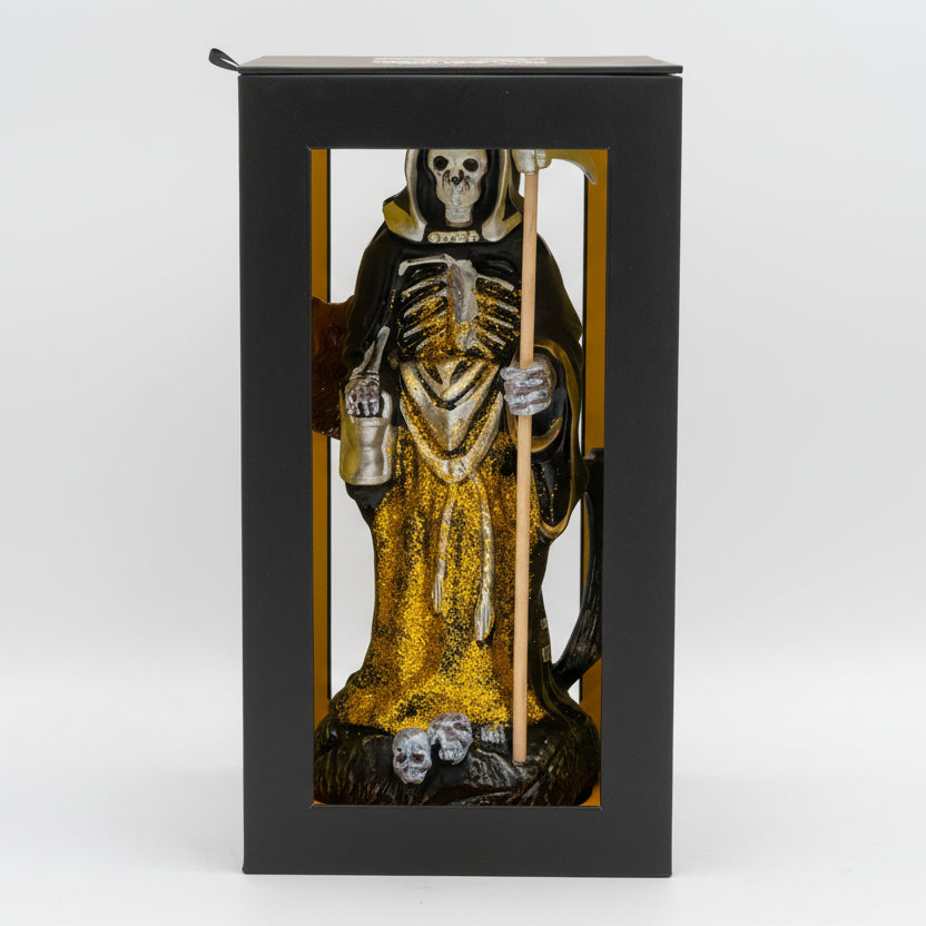 Statue of a skeleton in a robe with a staff inside a black box on a white background
