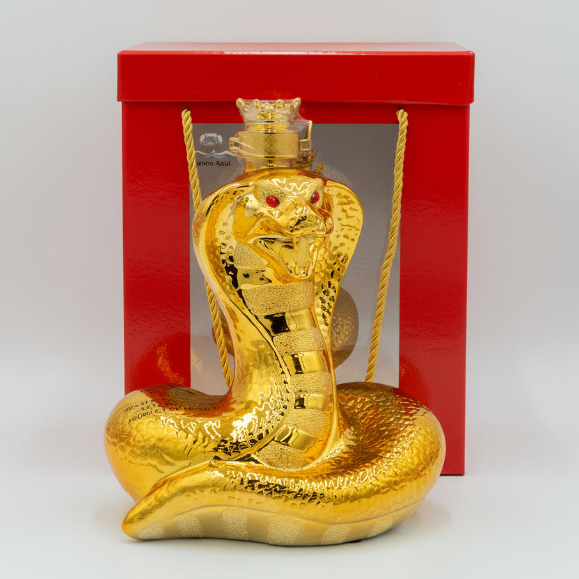 Gold snake-shaped bottle with red eyes in front of a red box on a white background