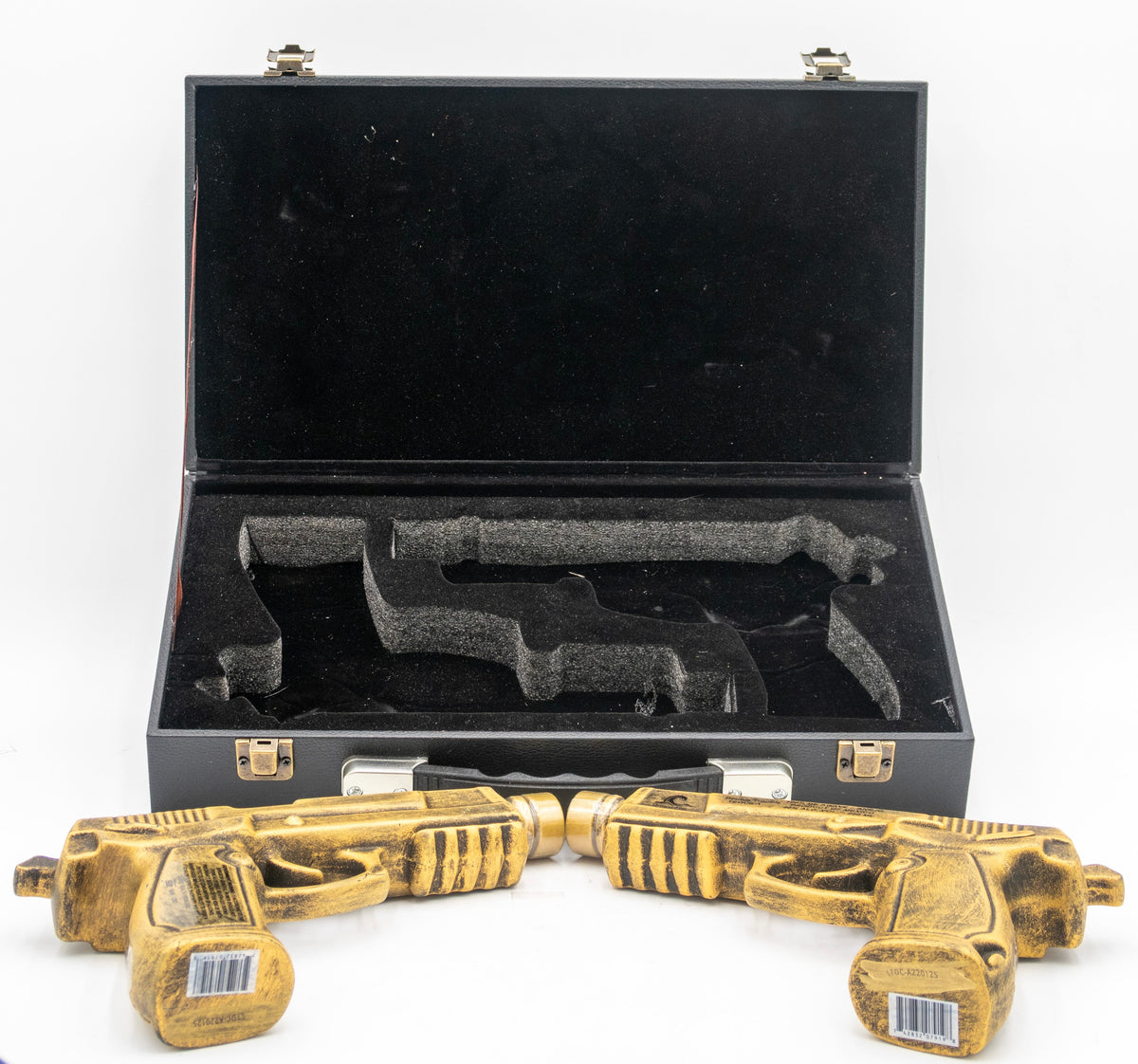 Two gold toy guns in front of an open black case on a white background